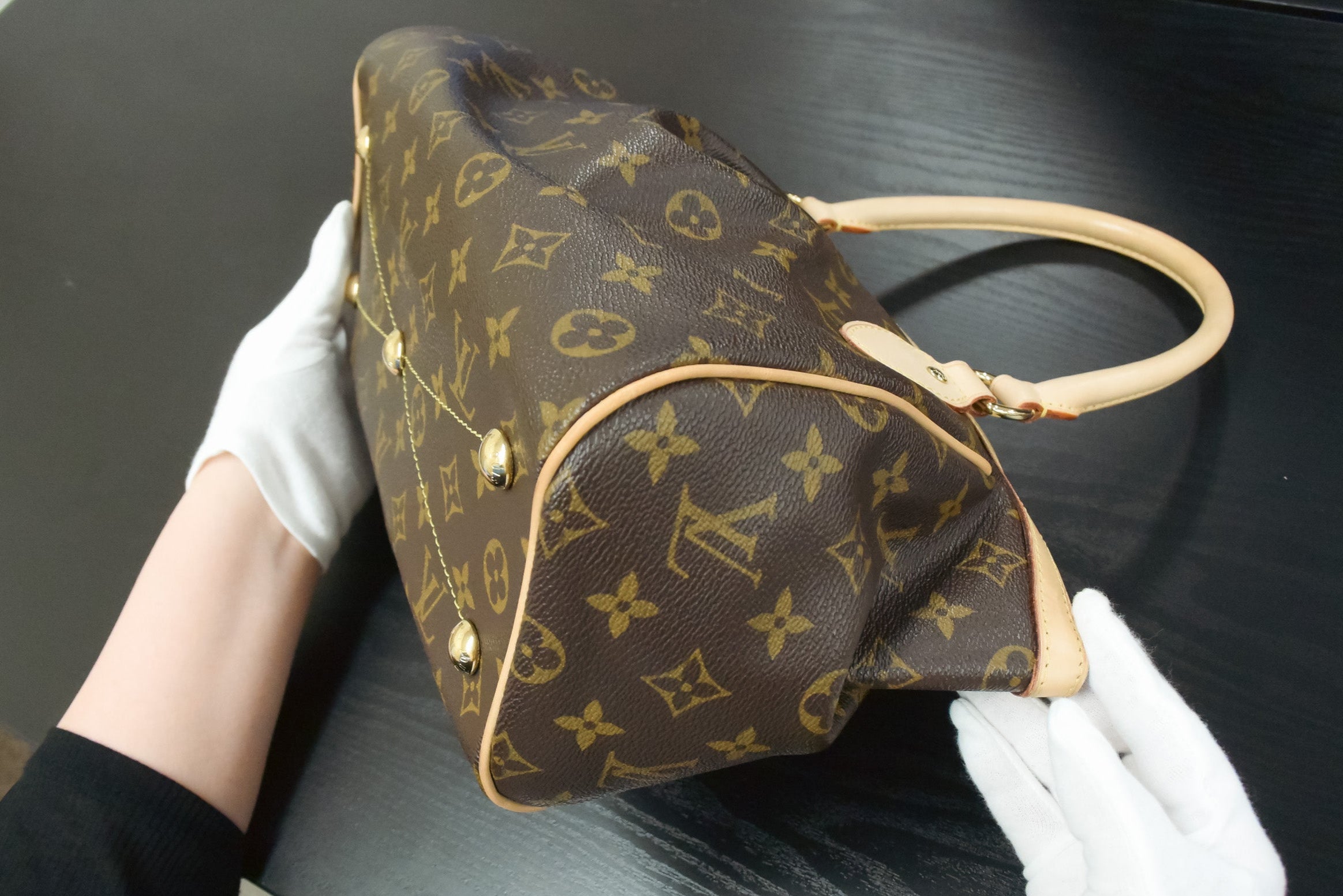 Louis Vuitton handbag held by a person wearing white gloves on a dark surface