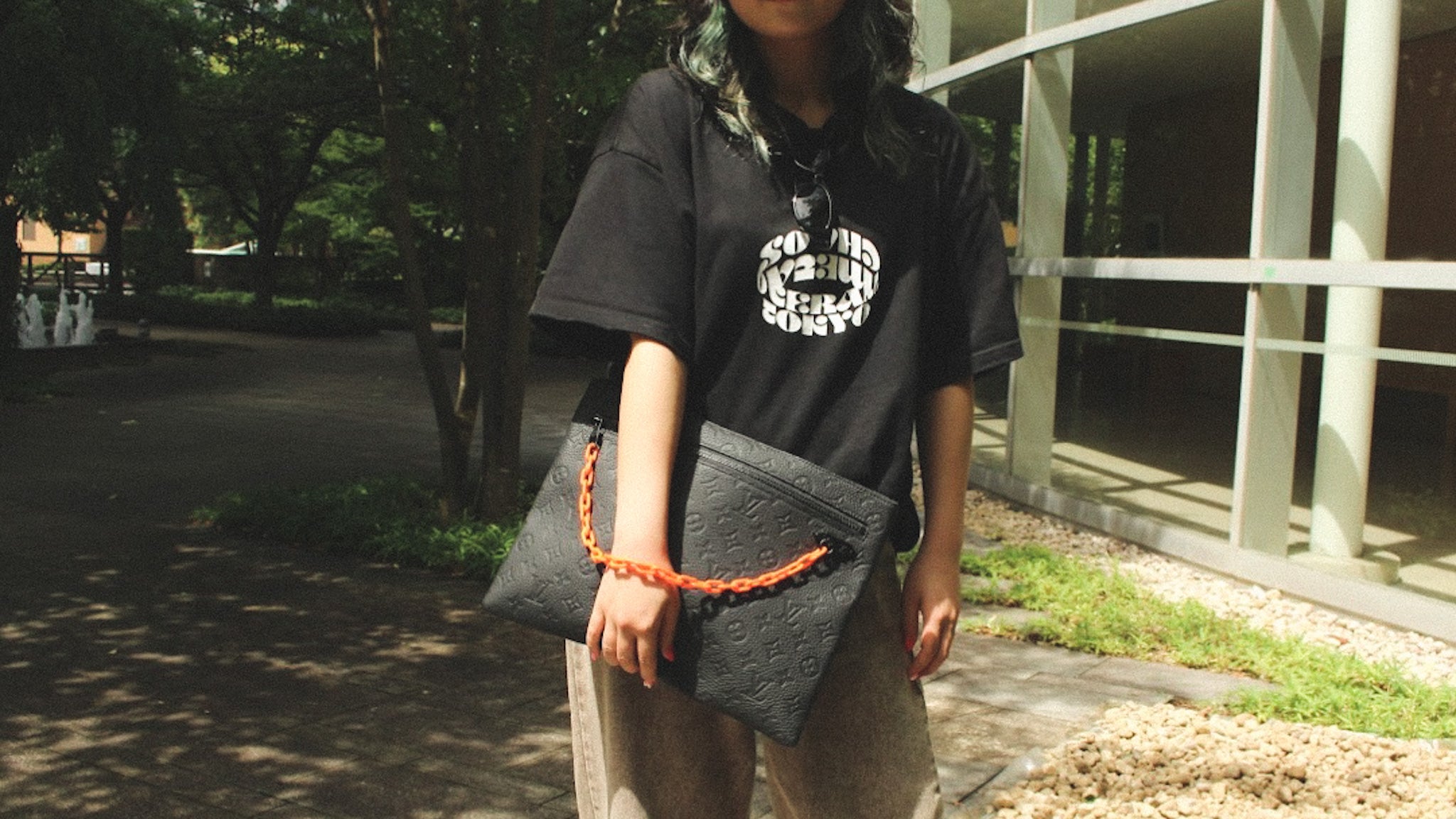 Person holding a black clutch with an orange strap outdoors