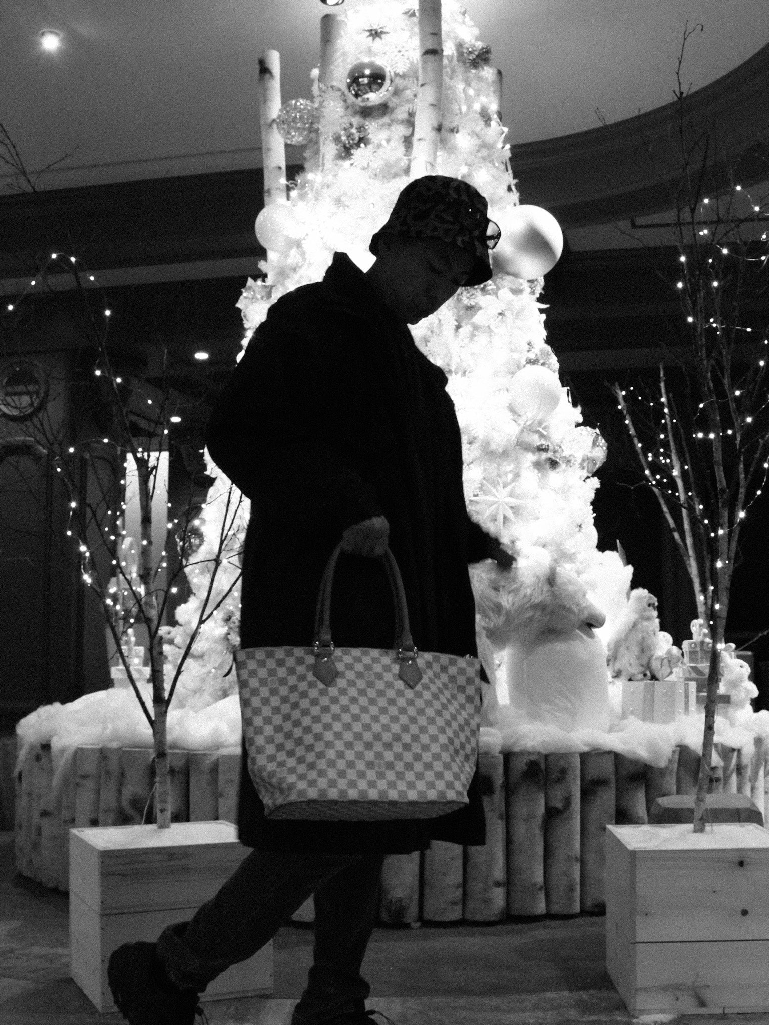 Person walking in front of a decorated Christmas tree with lights.